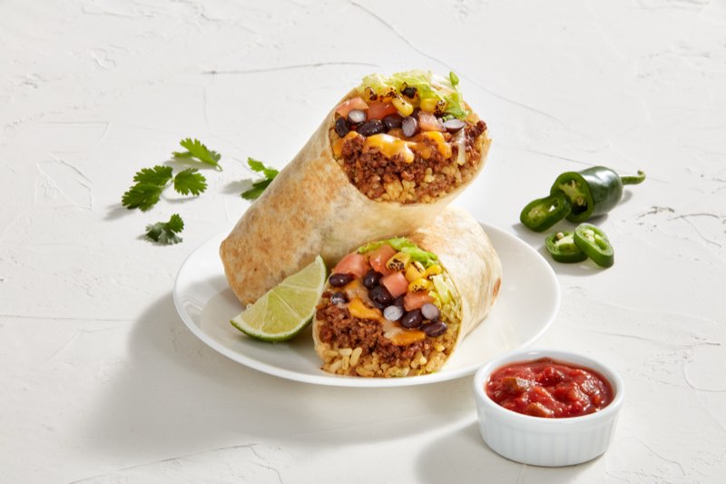 Burrito cut in half showing rice, beef, black beans, corn and cheese, with salsa and lime