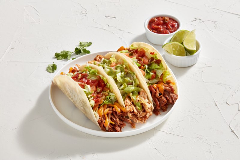 Three pulled pork and chicken tacos with salsa and lime